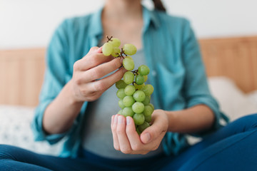Cropped photo of young pregnant woman eating grapes in bed .