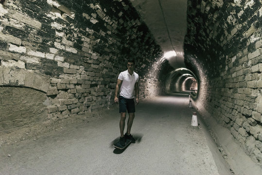 Young 20-25 years old man in tunnel with skateboard. Ambient light image (IMAGE HAVE SOME NOISE)