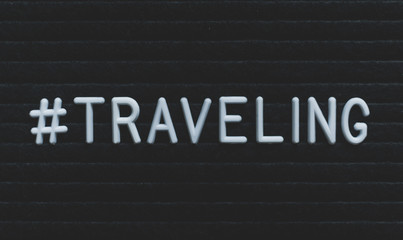 Hashtag word #traveling written on the letter board. White letters on the black background.