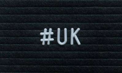 Hashtag word #uk written on the letter board. White letters on the black background.