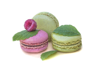 Pink and green pastel colored macaroons with raspberry and mint leaves on white background