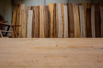 A selection of high quality, premium wood planks and slabs. Vertical timber elements over concrete industrial wall in a massive carpentry facility. Italy, Rome 2018.