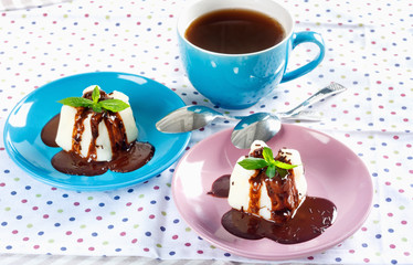 Cream pudding with chocolate sauce, mint and cup of tea on multicolored tablecloth.