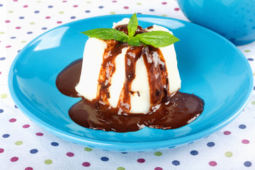 Cream pudding with chocolate sauce and mint on  multicolored tablecloth.
