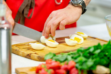 Man cuts boiled quail eggs on wooden cutting board close-up. Step by step recipe of homemade dish