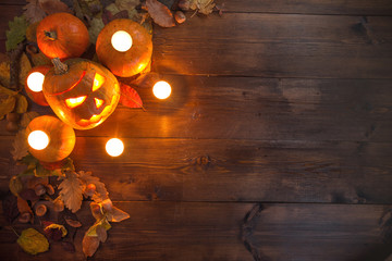 concept of Hallowen, autumn still life of small pumpkins that lie on dry leaves on a dark wooden background at the upper left border of the frame with burning candles laid out on the same pumpkins. 