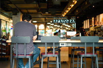 Portrait of unidentified man sitting on the high chair and working with his laptop at the coffee shop - obrazy, fototapety, plakaty