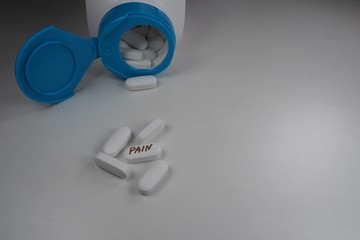 white oval tablet with the inscription "pain" and an open jar of tablets in the background