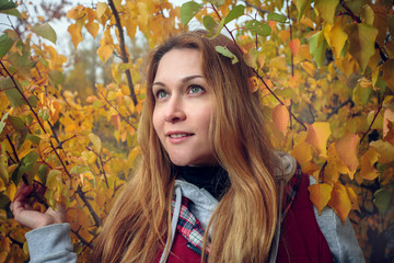 Naklejka na ściany i meble Portrait of a young blonde girl with green eyes and long hair in yellow autumn leaves. Close-up, flash light