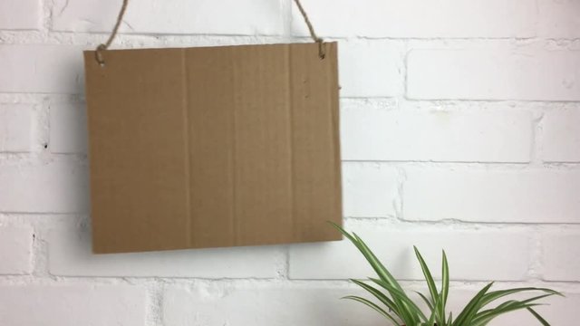 Cartel de carton balanceandose en un fondo de ladrillos blancos.