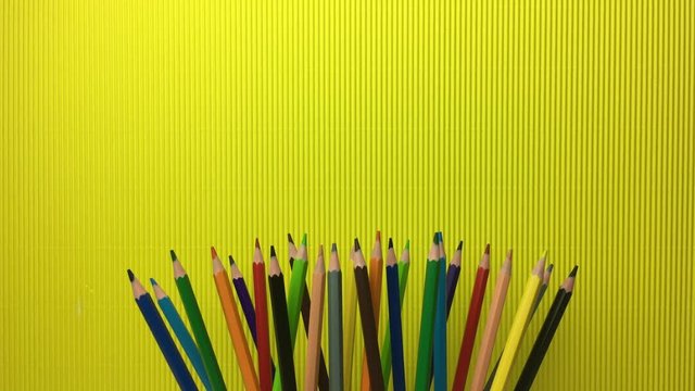 Lapices de colores acercandose, sobre fondo amarillo.