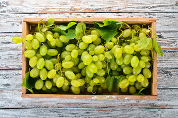 White Grapes in a wooden box on a white wooden table. Leaves of grapes. Top view. Free space for text.