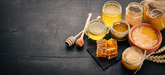 A set of honey and bee products. Honey in honeycomb. On a black wooden background. Free space for text. Top view. - obrazy, fototapety, plakaty