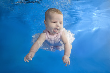 Fototapeta na wymiar Little girl in a pink dress swims underwater in the pool