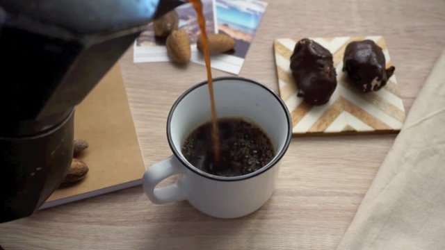Hot black coffee pouring from italian coffee maker to white cup on wooden table