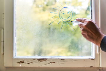 Fenster im Winter mit Eiskristallen, Mann malt eine Sonne darauf