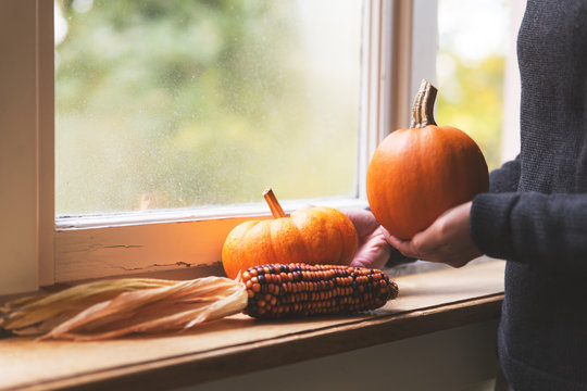 Frau dekoriert auf einer Fensterbank mit Kürbissen und Mais, Herbstdekoration