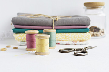 Vintage thread spools, little wooden buttons in jar, retro scissors and cotton fabrics on white