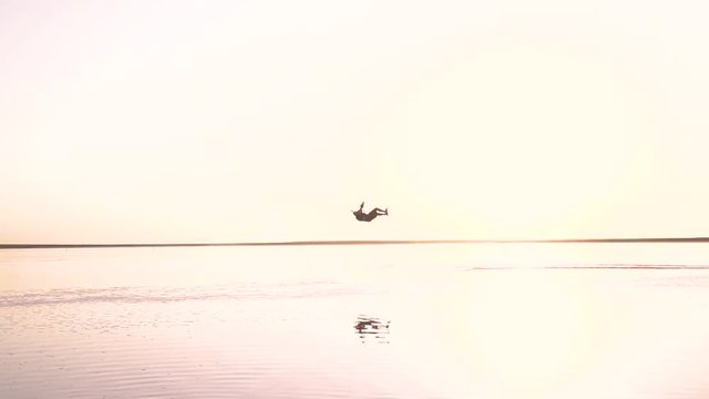 A man of kitesurfer at dawn performs tricks in the air, slow motion