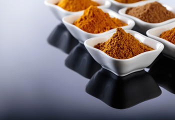 Small white ceramic bowls of Indian spices on black reflective background.