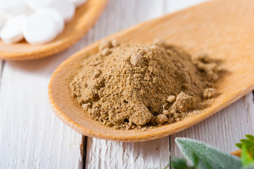 herbal leaves, ground herb powder and medicament pills on bamboo spoons, white wooden table