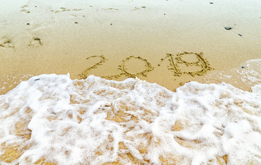 Inscription 2019 on the beach sand with a sea wave. New Year 2019 is coming concept. Background photography.