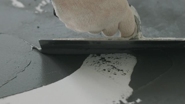 Slow motion closeup male worker applying micro concrete plaster coating on the floor with a trowel