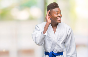 Young african american man over isolated background wearing kimono smiling with hand over ear listening an hearing to rumor or gossip. Deafness concept.