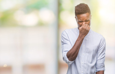 Young african american man over isolated background smelling something stinky and disgusting,...