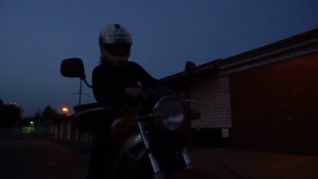 woman putting on helmet sit on motorcycle start an engine and go away to the night riding