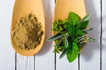 herbal leaves and ground herb powder on bamboo spoons, white wooden table