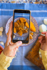 Woman hands takes photography of food on table with phone. Dinner, lunch. Baked, cooked pumpkin slices. Smartphone photo for social networks or blogging post. Vegetarian, healthy, organic