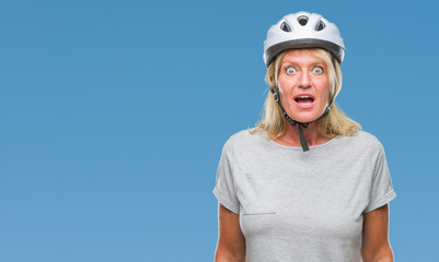 Middle age caucasian cyclist woman wearing safety helmet over isolated background afraid and shocked with surprise expression, fear and excited face.