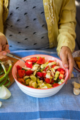 Young woman hands holds fresh summer vegetables salad with greens, tomatoes, onion rings, olive oil, spices and herbs in a bowl. Vegan light appetizer, healthy vegetarian food
