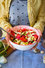 Young woman hands holds fresh summer vegetables salad with greens, tomatoes, onion rings, olive oil, spices and herbs in a bowl. Vegan light appetizer, healthy vegetarian food