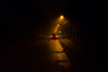 A car driving away under streetlamps a misty night