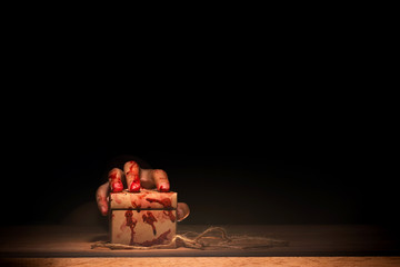 bloody hand holding a box on wooden table in horror and mysterious concept