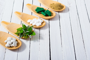 Obraz na płótnie Canvas herbal leaves, ground herb powder and medicament pills on bamboo spoons, white wooden table