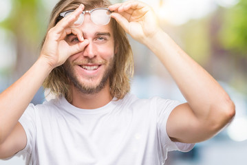 Young handsome man with long hair wearing glasses over isolated background doing ok gesture with hand smiling, eye looking through fingers with happy face.