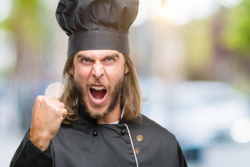 Young handsome cook man with long hair over isolated background angry and mad raising fist...