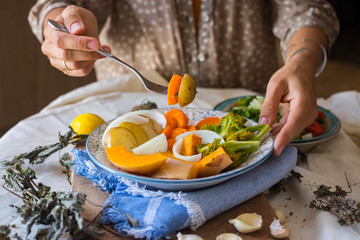 Woman hands holds steamed cooked assorted vegetables. Carrots, pumpkin, roasted potato, onion rings, broccoli. Seasonal vegan lunch, vegetarian autumn dinner, healthy food. With herbs, spices.