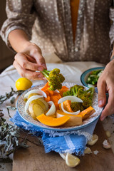 Woman hands holds steamed cooked assorted vegetables. Carrots, pumpkin, roasted potato, onion rings, broccoli. Seasonal vegan lunch, vegetarian autumn dinner, healthy food. With herbs, spices.