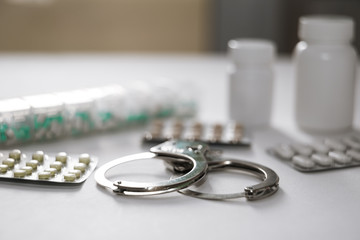 Handcuffs and pills and drugs on white table. Selective focus