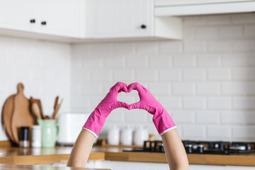 Heart made of pink protective gloves on white kitchen background.. Woman hands wearing protective...