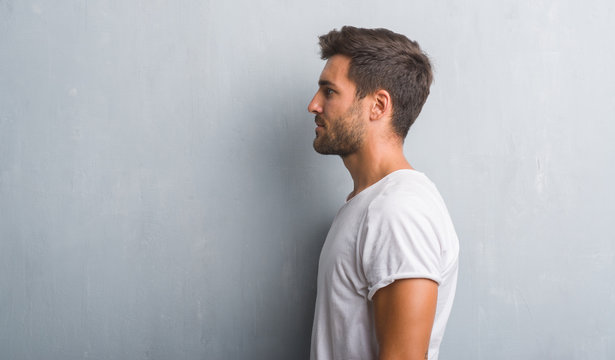 Handsome young man over grey grunge wall looking to side, relax profile pose with natural face with confident smile.