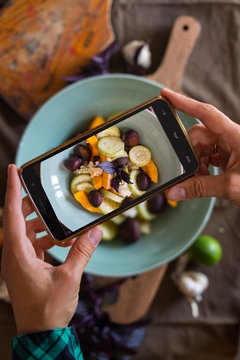 Woman hands takes photography of food on table with phone. Dinner, lunch. Roasted vegetables with fried chestnuts. Smartphone photo for social networks or blogging post. Vegetarian, healthy, organic