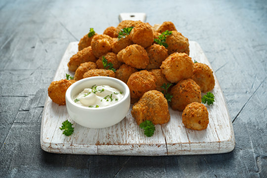 Homemade Breaded Garlic Mushrooms with sour cream and parsley on white wooden board
