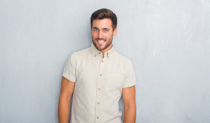 Handsome young man over grey grunge wall wearing summer shirt looking away to side with smile on face, natural expression. Laughing confident.
