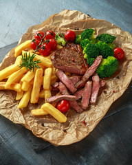 Grilled sirloin steak with potato fries, broccoli and cherry tomatoes on crumpled paper