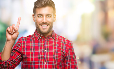 Obraz premium Young handsome man over isolated background showing and pointing up with finger number one while smiling confident and happy.